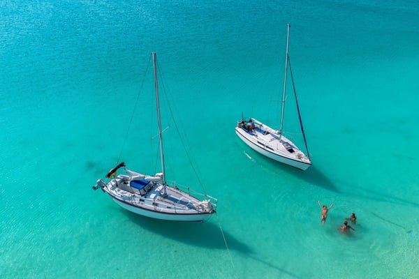 Two white sailboats anchored in the turquoise waters of Bacalar lagoon with swimmers nearby