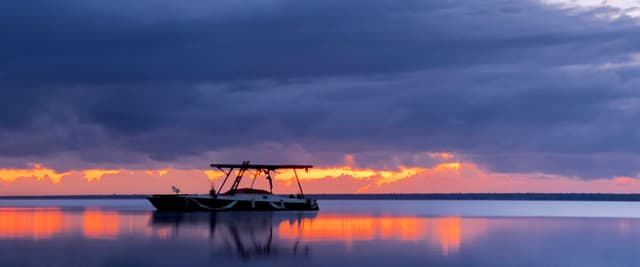 Boat silhouetted on Bacalar lagoon at purple and orange sunset