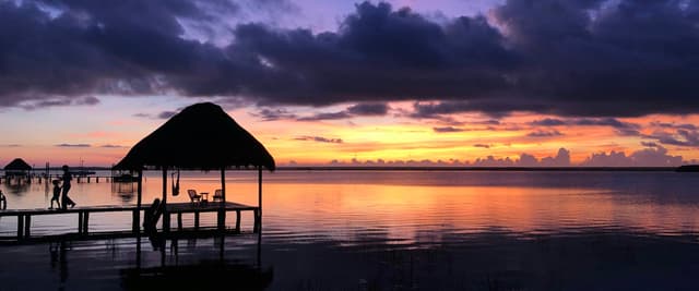 Palapa hut silhouetted on the Bacalar lagoon at purple-gold sunset
