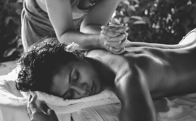 Outdoor massage in Mexico, therapist working on a man's back with tropical foliage behind