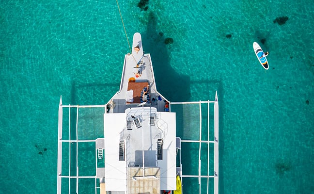 Aerial view of a white catamaran anchored in turquoise water with paddleboards nearby