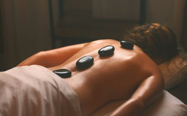 Person lying on a massage table with hot stones placed along their back
