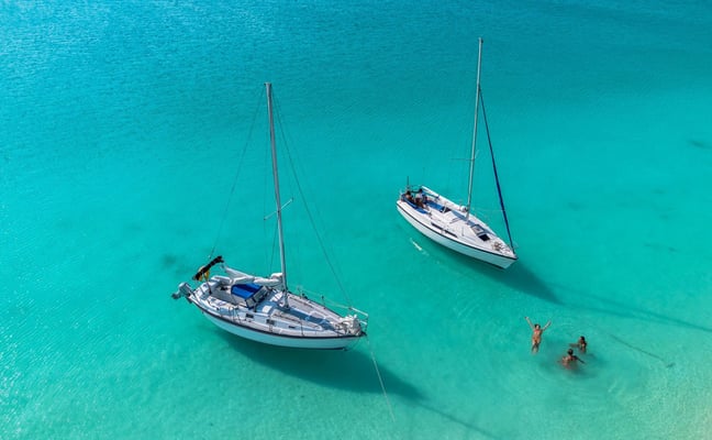 Two white sailboats anchored in the turquoise waters of Bacalar lagoon with swimmers nearby