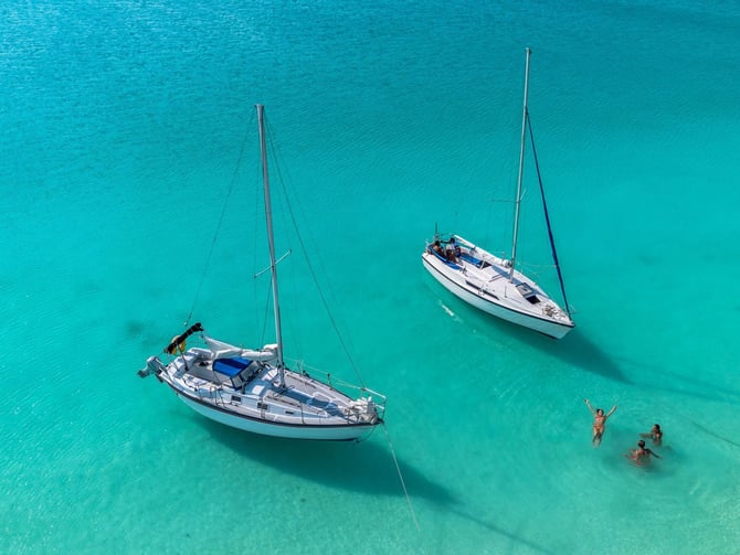 Two sailboats anchored in turquoise water near three people swimming.