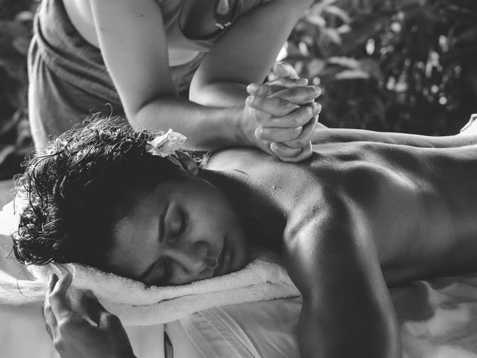 Outdoor massage in Mexico, therapist working on a man's back with tropical foliage behind