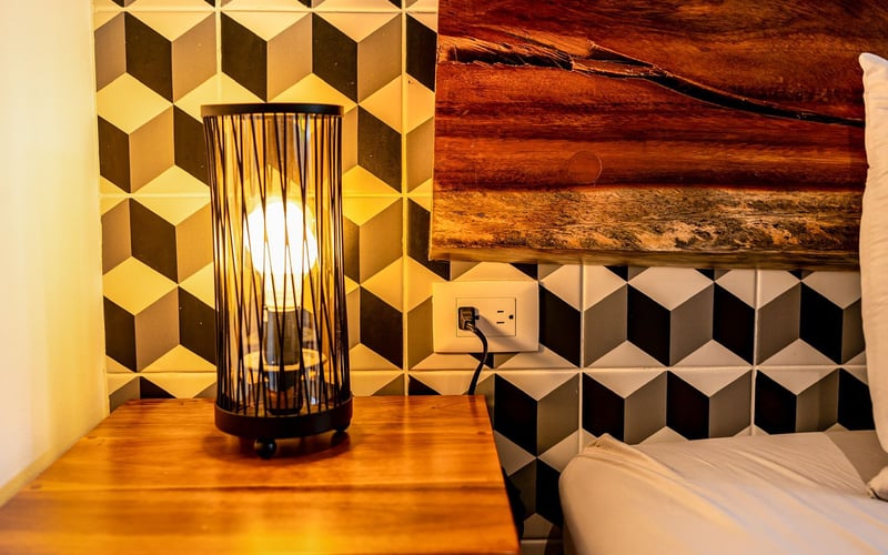 Nightstand with lamp, geometric tile wall, and artwork.