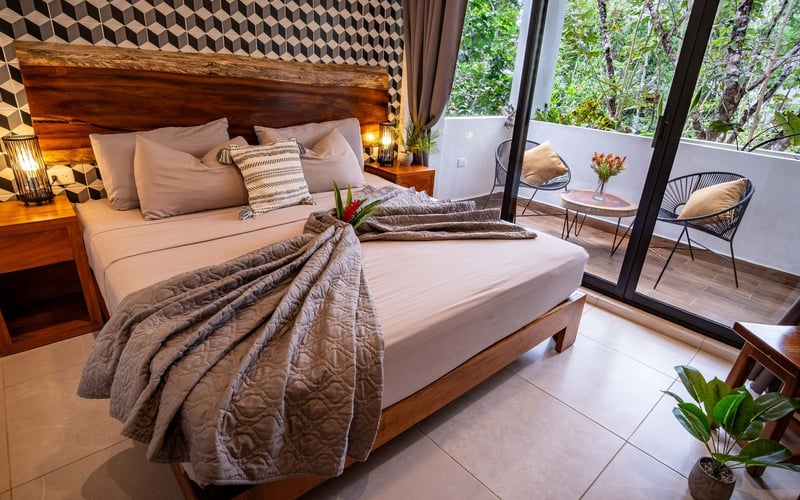 Bedroom with bed, balcony, wooden headboard, geometric patterned wallpaper.